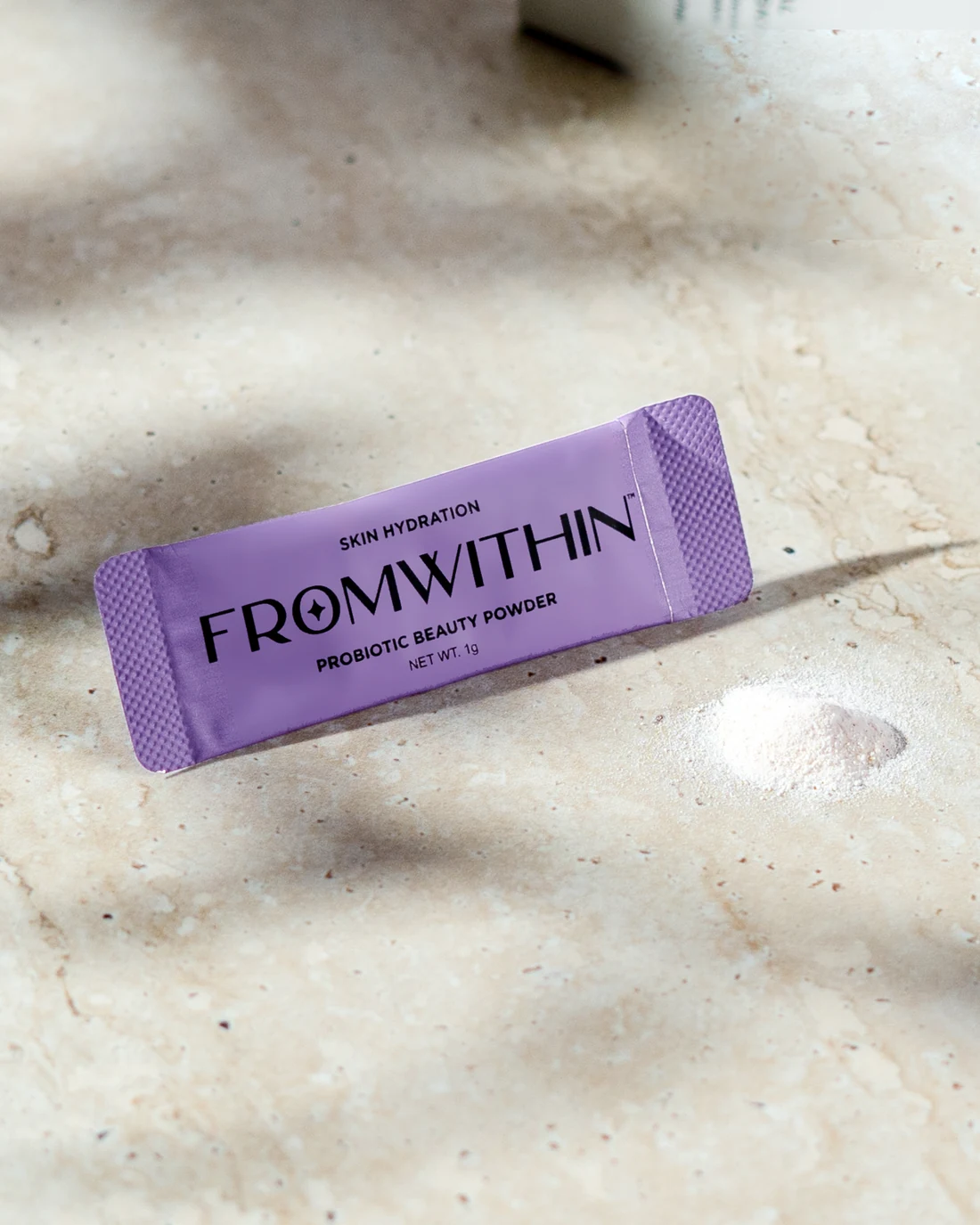 A FROMWITHIN sachet and a small mound of powder on travertine in soft light