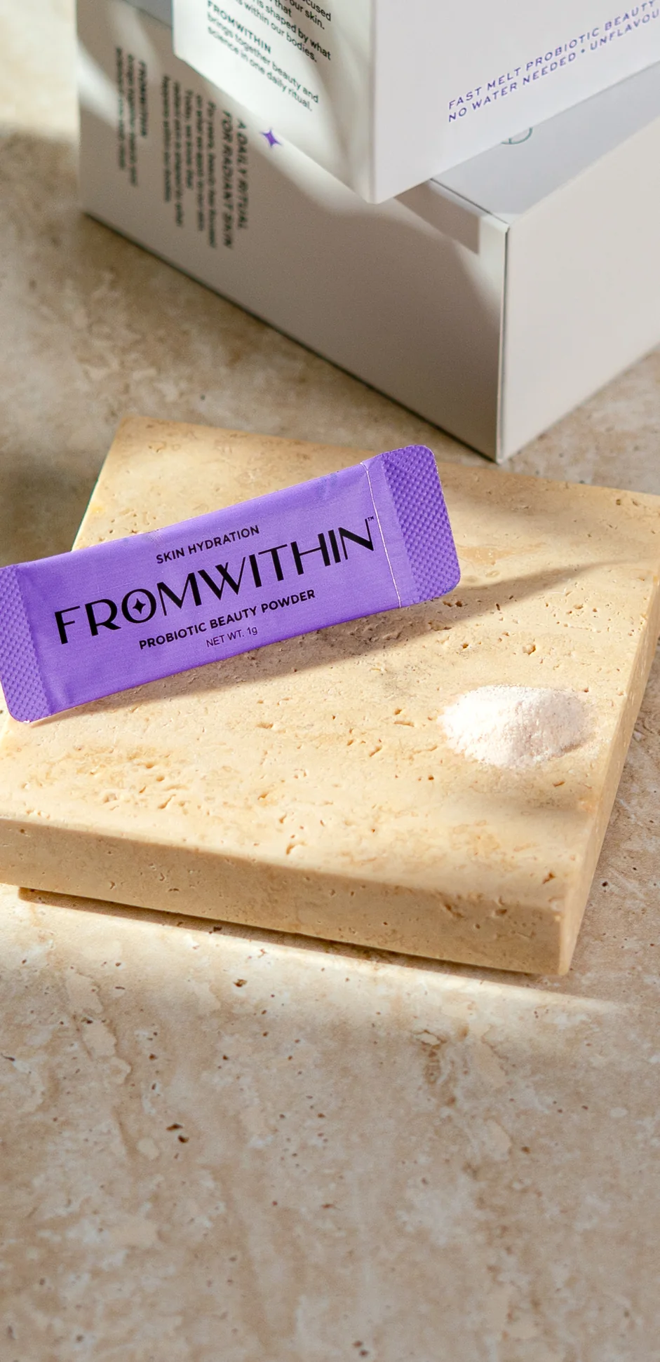 A FROMWITHIN sachet on a travertine slab beside the box in warm sunlight